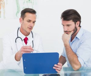 Male,Doctor,Discussing,Reports,With,Patient,At,Desk,In,Medical